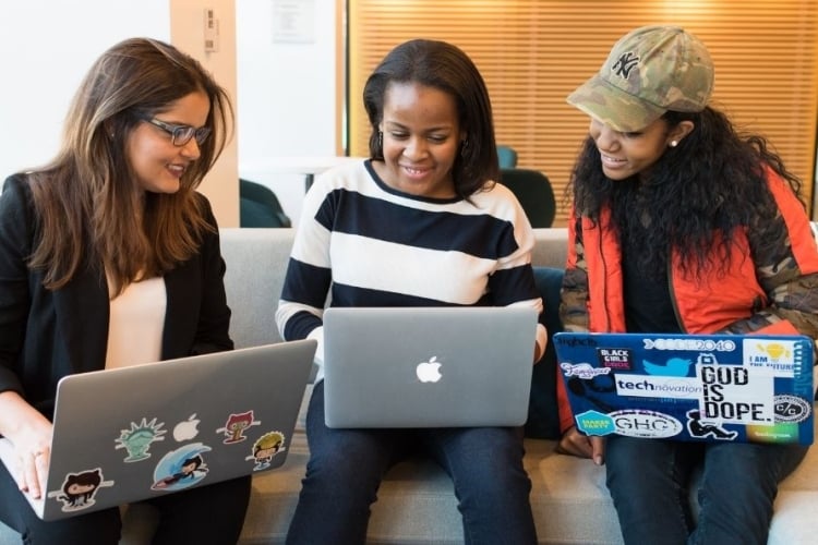 Tres mujeres con una computadora cada una observando la portatil de la que se encuentra en el medio de ellas.