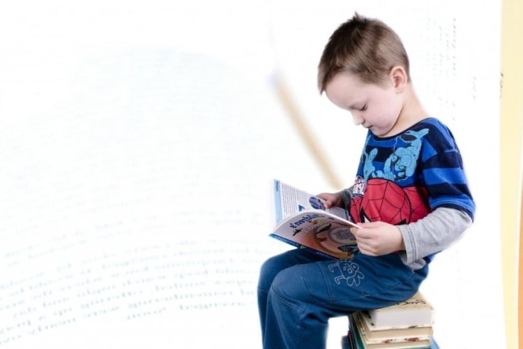 Niño sobre una pila de libros leyendo un libro