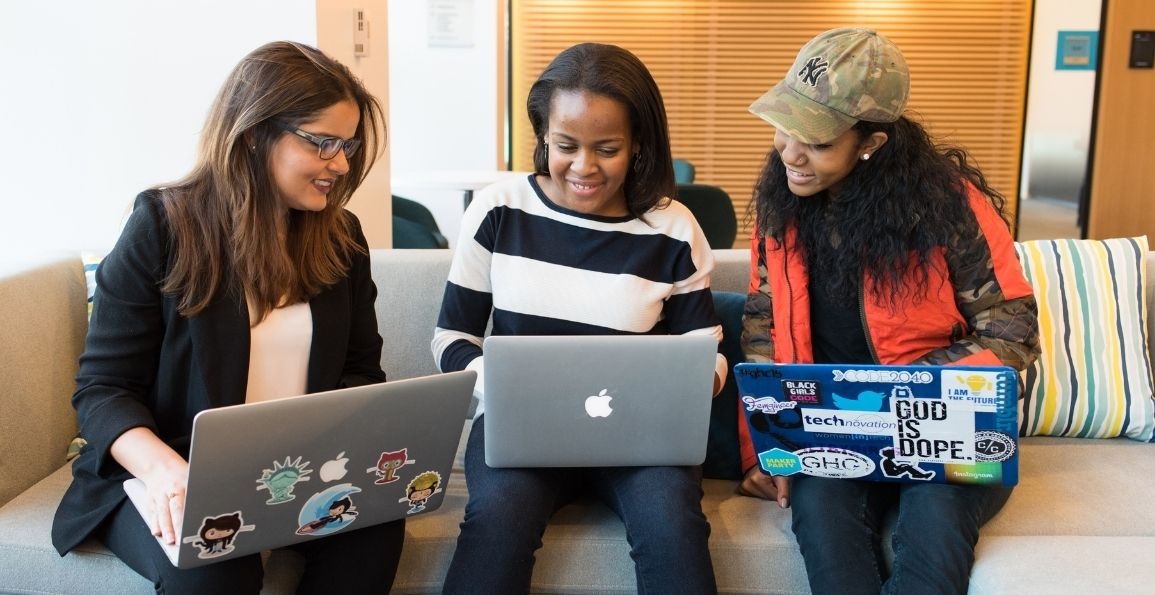 Tres mujeres con una computadora cada una observando la portatil de la que se encuentra en el medio de ellas.