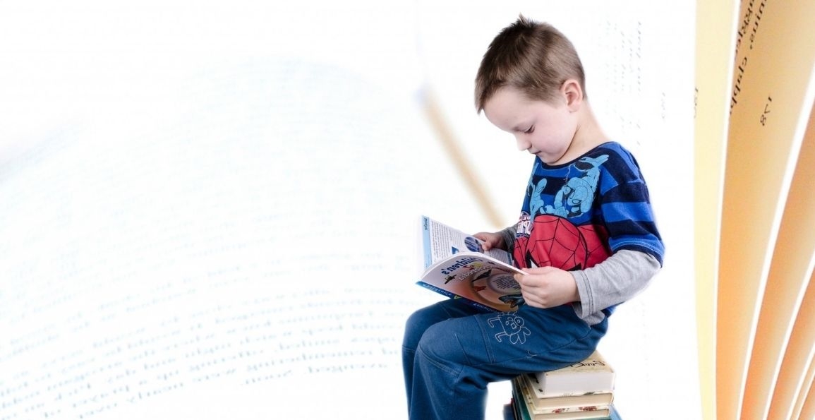 Niño sobre una pila de libros leyendo un libro